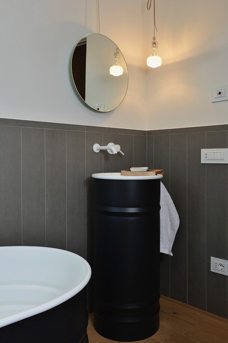 Modernisiertes Bad mit grauer Wandverkleidung, rundem Spiegel und schwarzem Waschbeckenmöbel