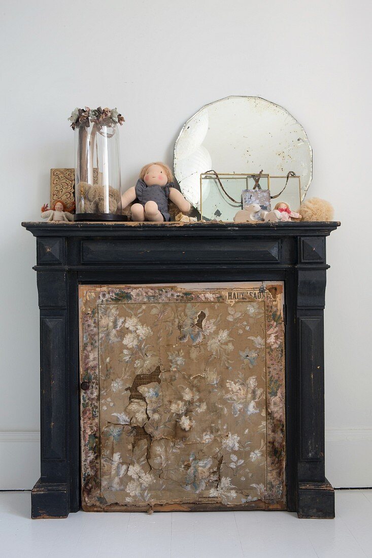 Torn fire screen in front of old fireplace with vintage ornaments on mantelpiece