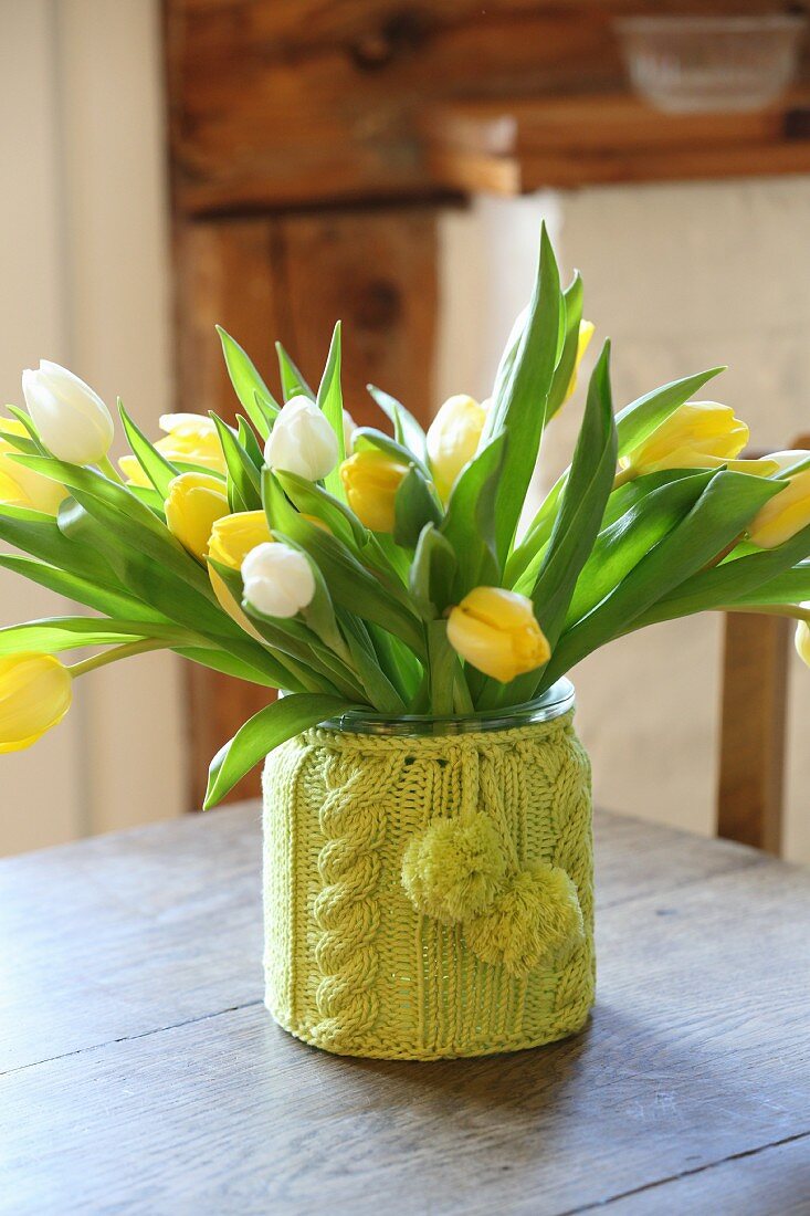 Tulpenstrauß in umstrickter Vase auf einem alten Holztisch