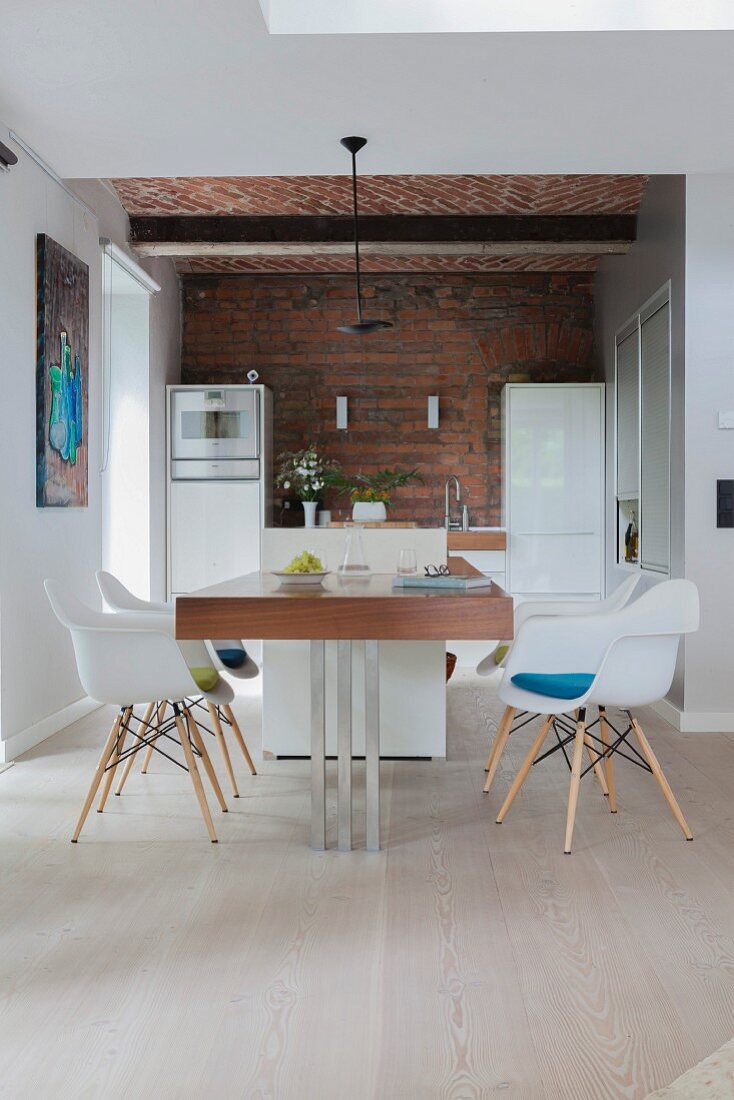 Modern dining table in open-plan kitchen with brick wall and vaulted ceiling