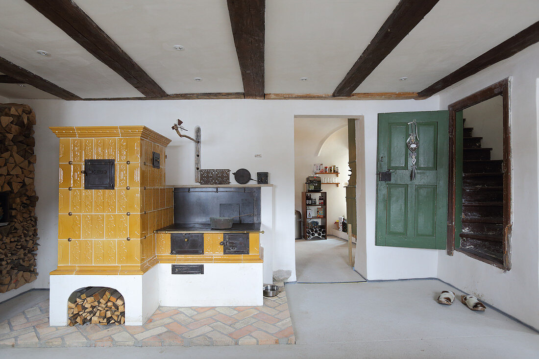 Old yellow tiled stove and wood-fired cooker next to doorway leading to stairs