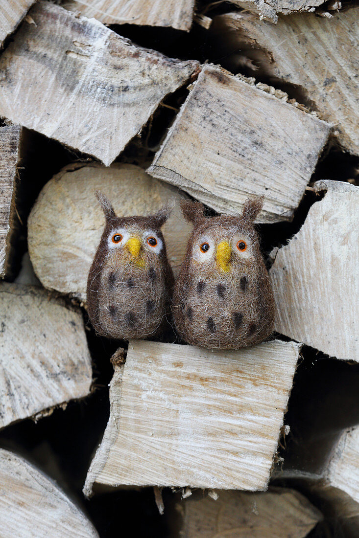 Hand-made, needle-felted, woollen owls on stacked firewood
