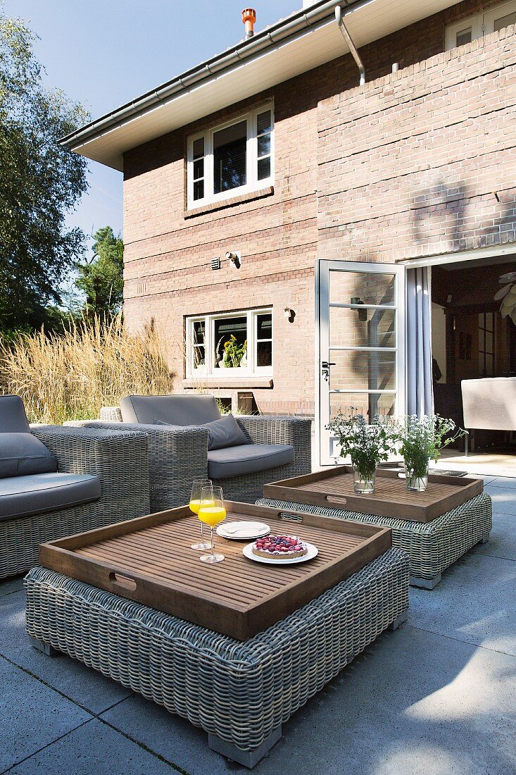 Lounge armchairs and tray tables on terrace outside brick house