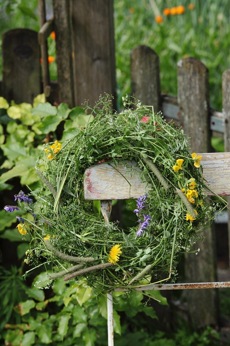 Wiesenblumenkranz an Vintage Gartenstuhl vor verwittertem Lattenzaun