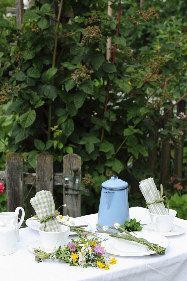 Set garden table decorate with posy of colourful wildflowers and pale blue enamel coffee pot