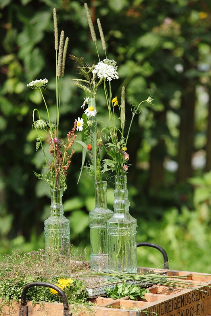 Nostalgische Glasflaschen mit Wiesenblüten und Grashalmen auf Vintage Holzkasten