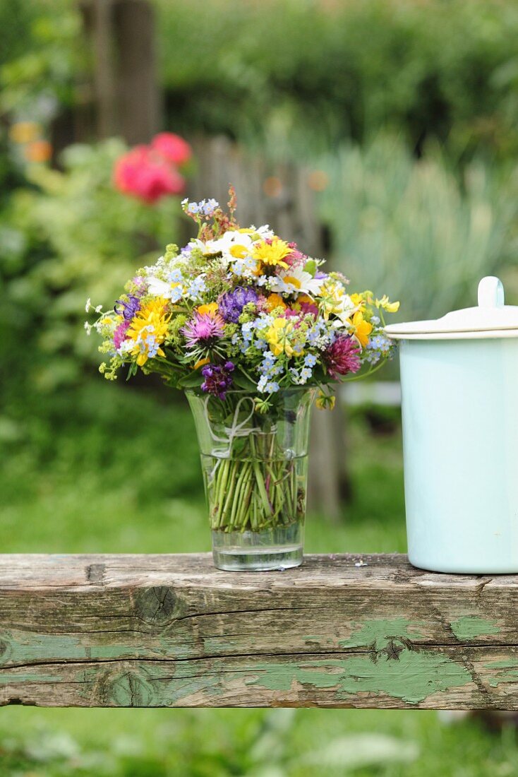 Vase of colourful wildflowers on vintage wooden beam in garden