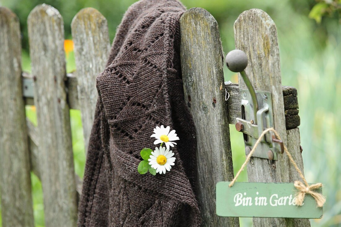 Flowers pinned to cardigan hung from vintage garden gate next to sign