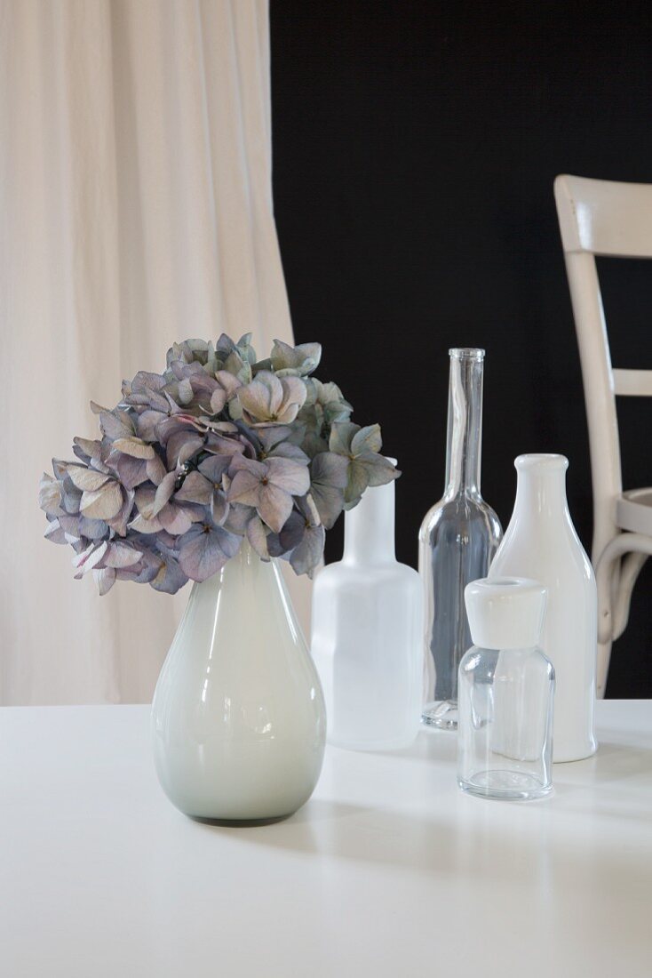 Vasensammlung mit pastellblauer Hortensienblüte auf weißem Tisch