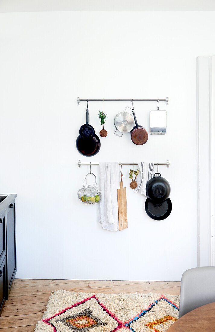 Pots and pans hung from metal rods on white kitchen wall