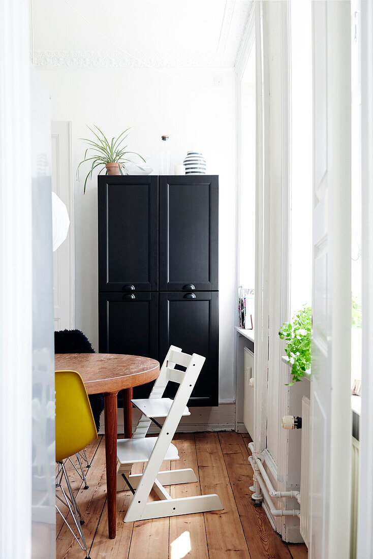 High chair at wooden table next to window and black wall-mounted cabinet in dining area