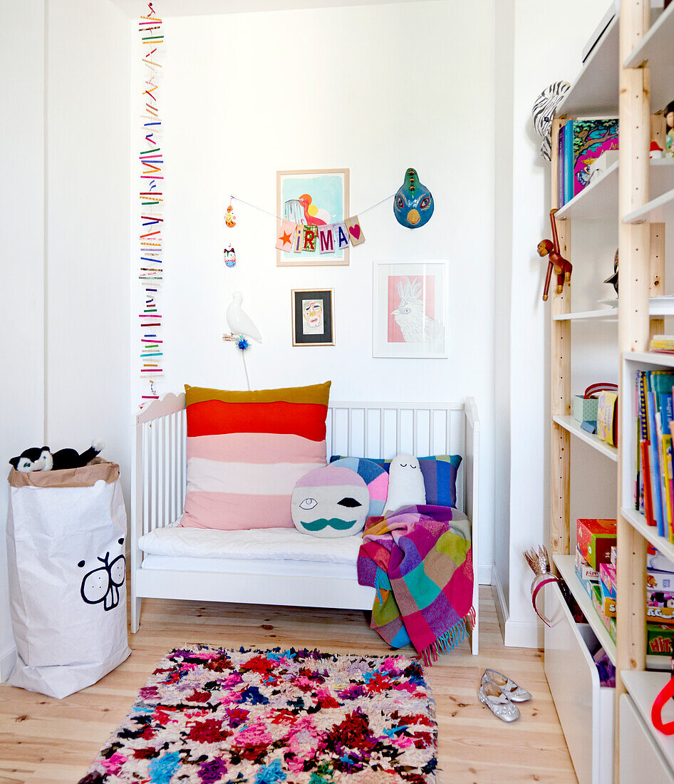 White couch with colourful cushions, shelves and colourful rug in child's bedroom