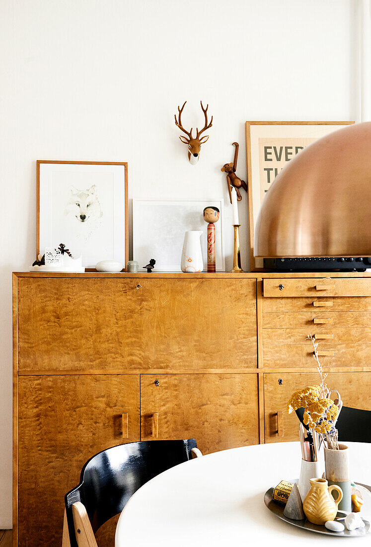 Ornaments on large wooden sideboard behind round table and black chairs