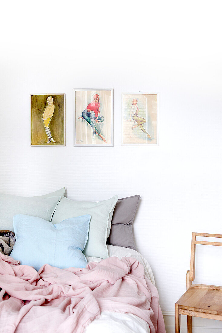 Three fashion plates on wall above bed with pastel bed linen