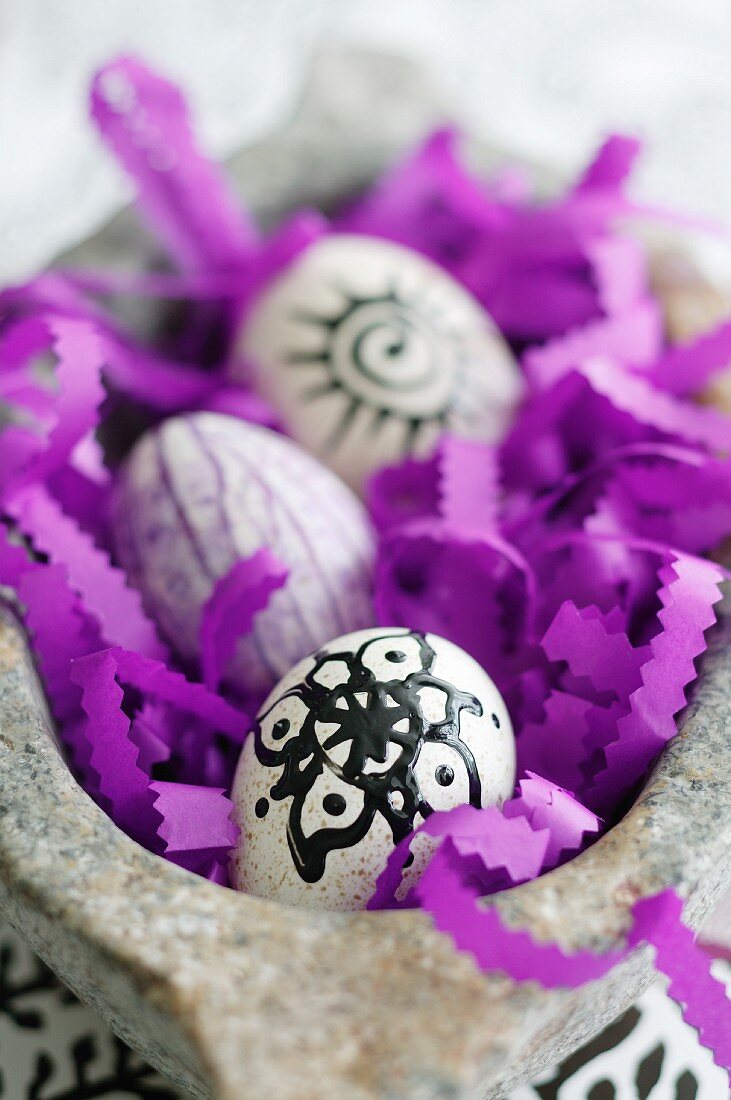 Decorated Easter eggs and purple paper strips with zigzag edges in stone bowl