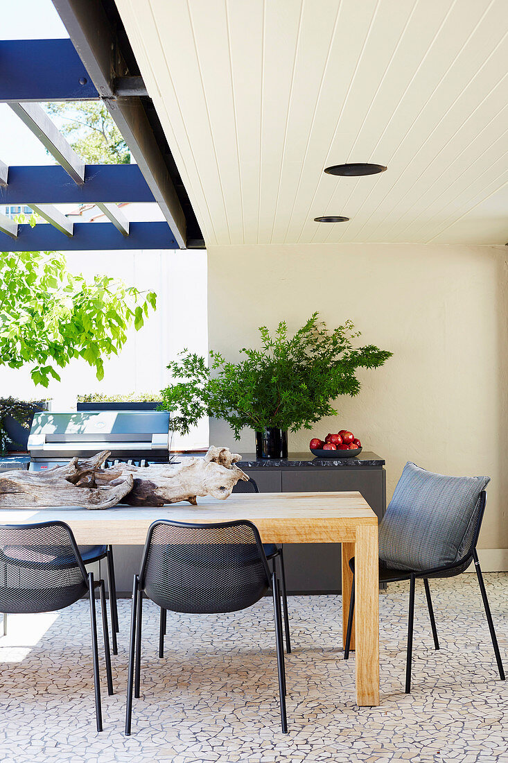 Esstisch auf überdachter Terrasse mit Outdoor-Küche und Grill