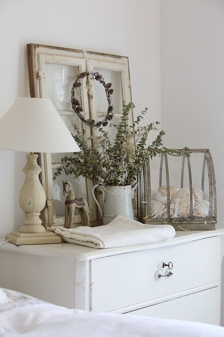 Table lamp, old window and vintage ornaments on chest of drawers