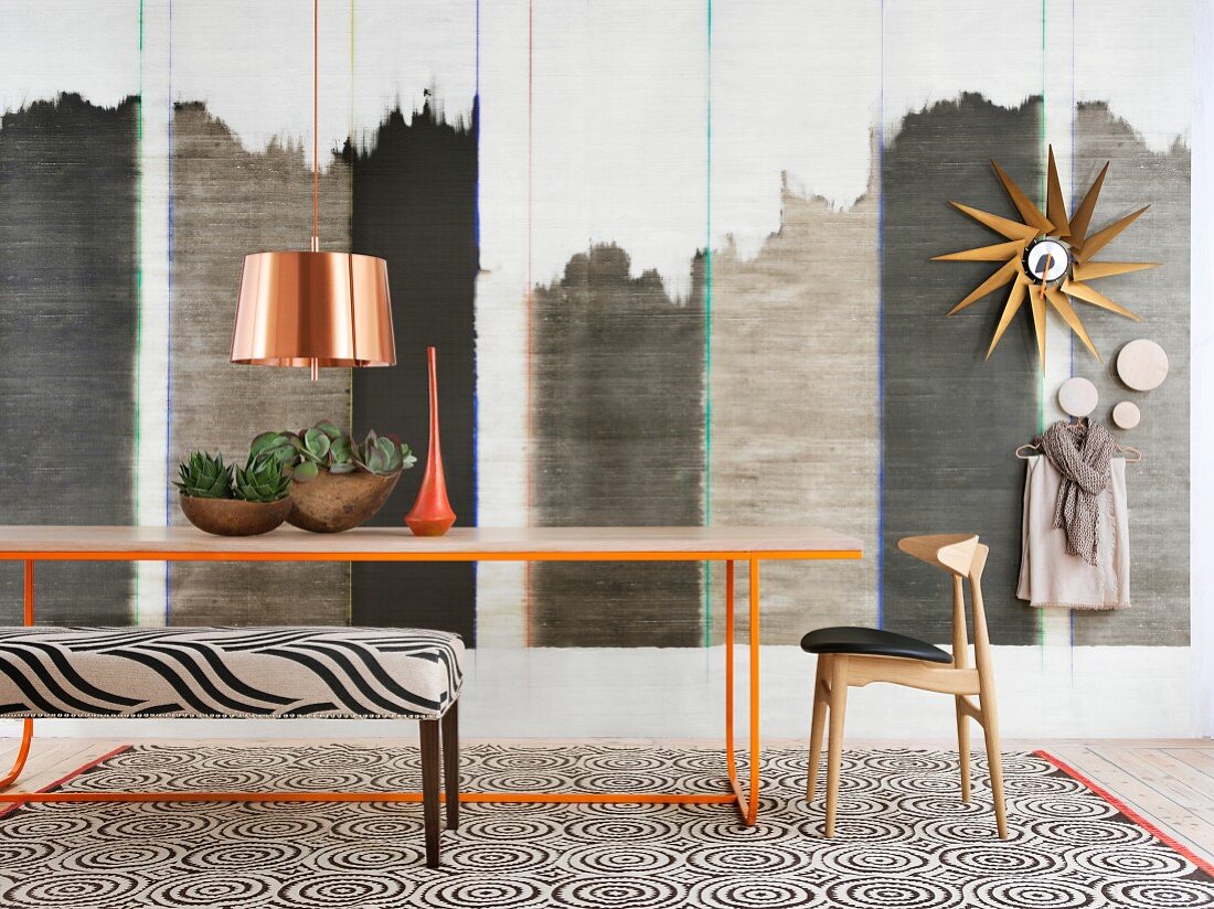 Filigranes, orangefarbenes Metall-Tischgestell vor Wandgestaltung im Ethno-Stil