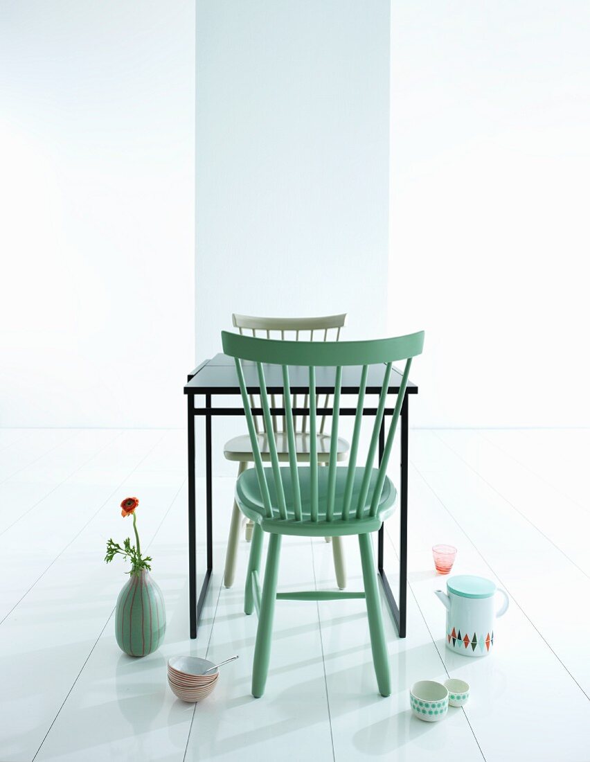 Mintgrüner Holzstuhl an schwarzem Tisch und Geschirr mit Retro Flair auf weißem Boden arrrangiert
