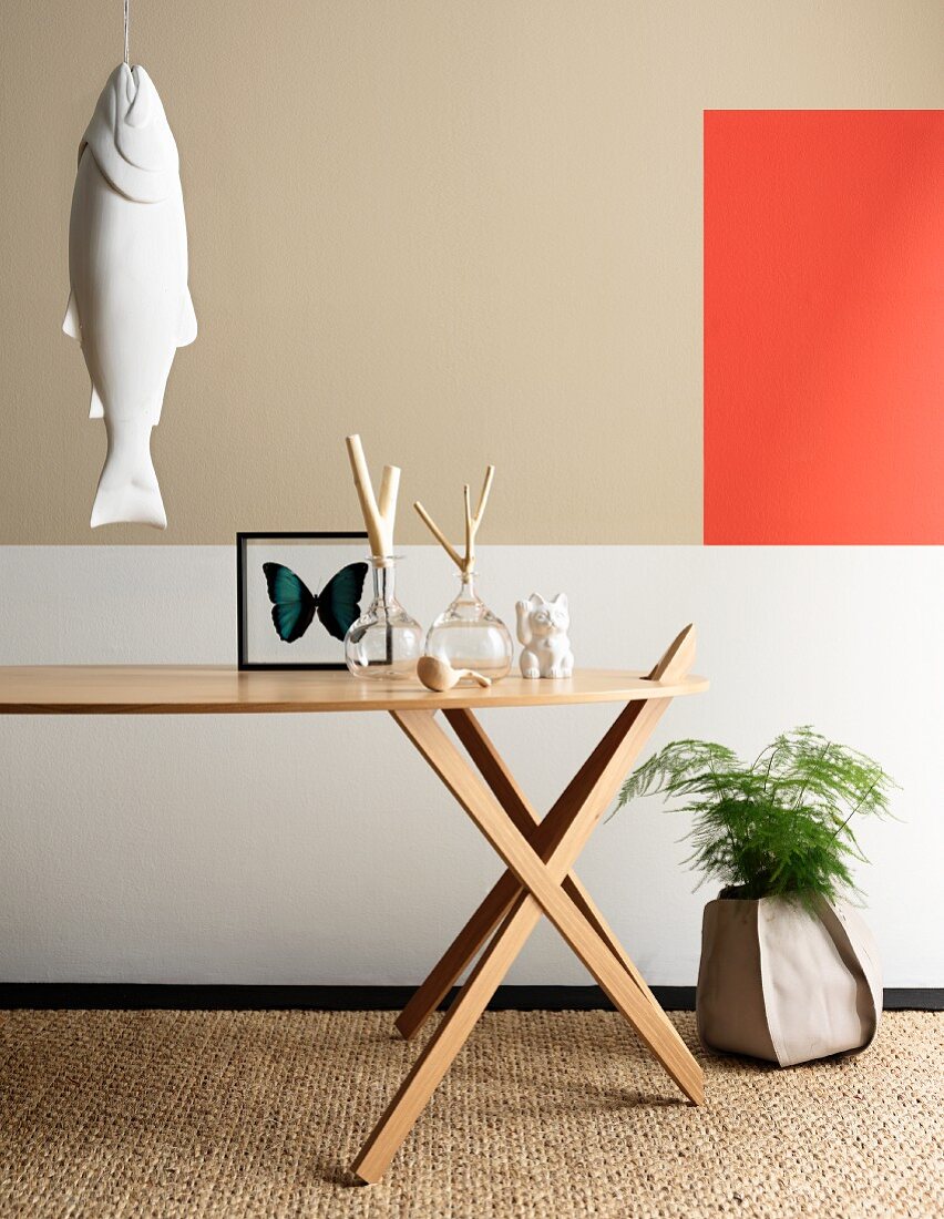 Designertisch mit Dekoobjekten und aufgehängte Fischskulptur vor geometrischer Wandgestaltung mit Farbakzent