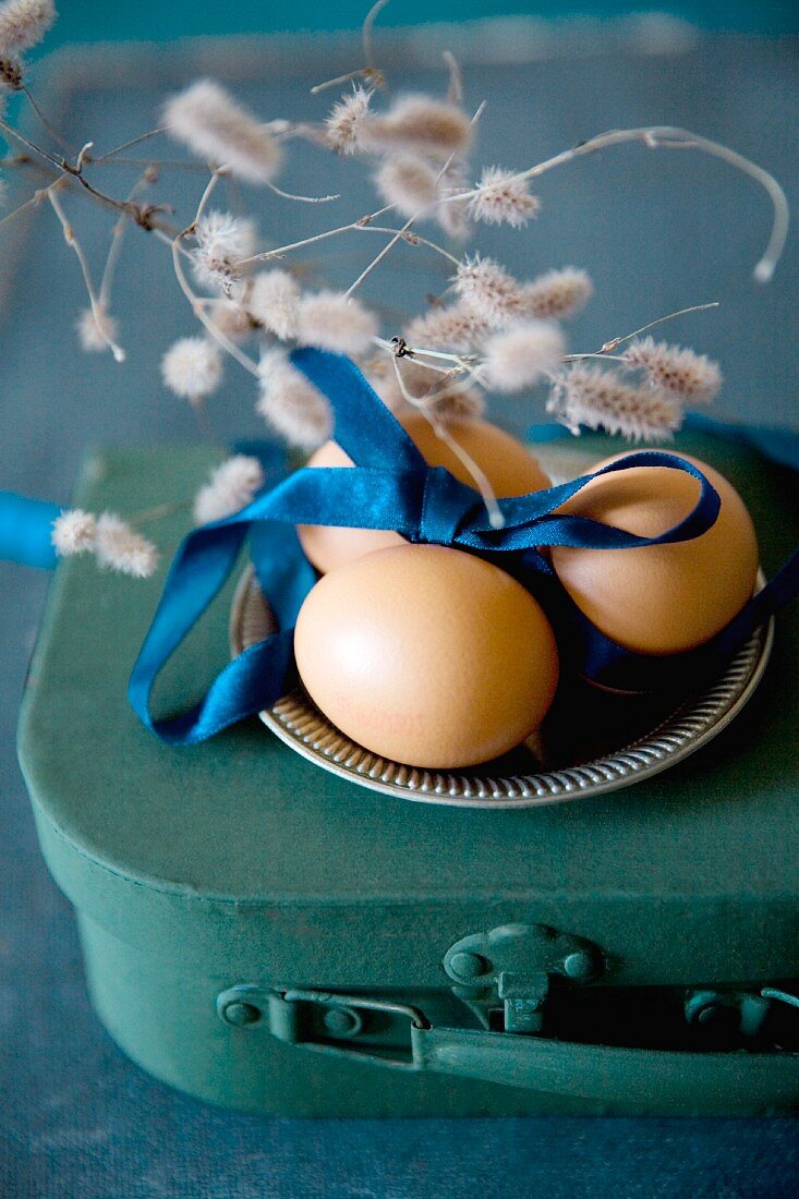 Kleiner Koffer mit Zinnteller und Eiern mit blauem Satinband