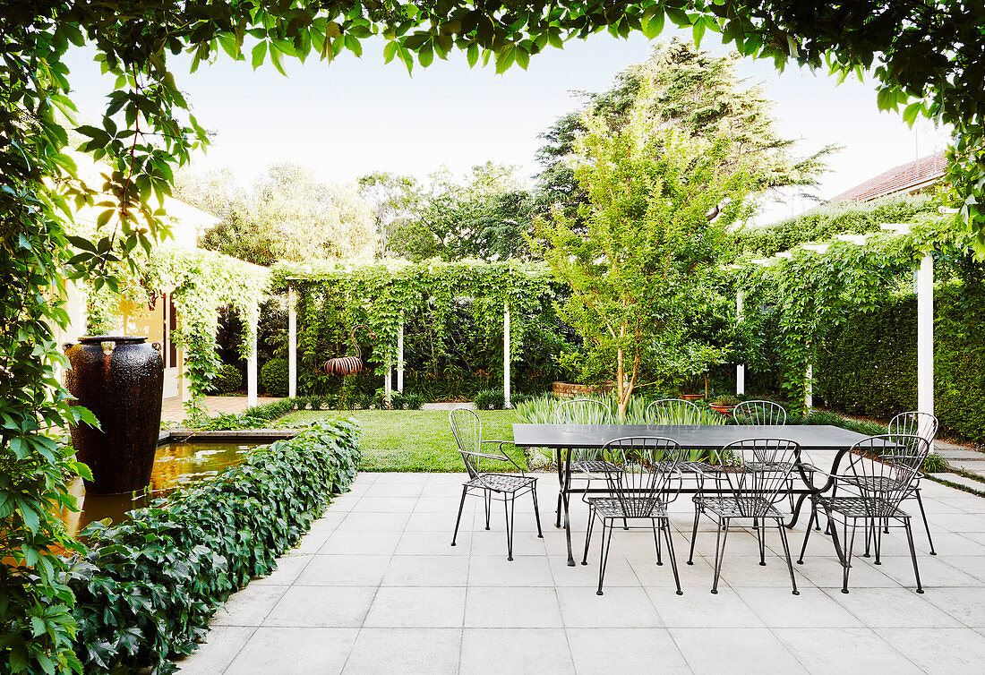 Terrace area with table and chairs made of metal, surrounded by green plants and lawn
