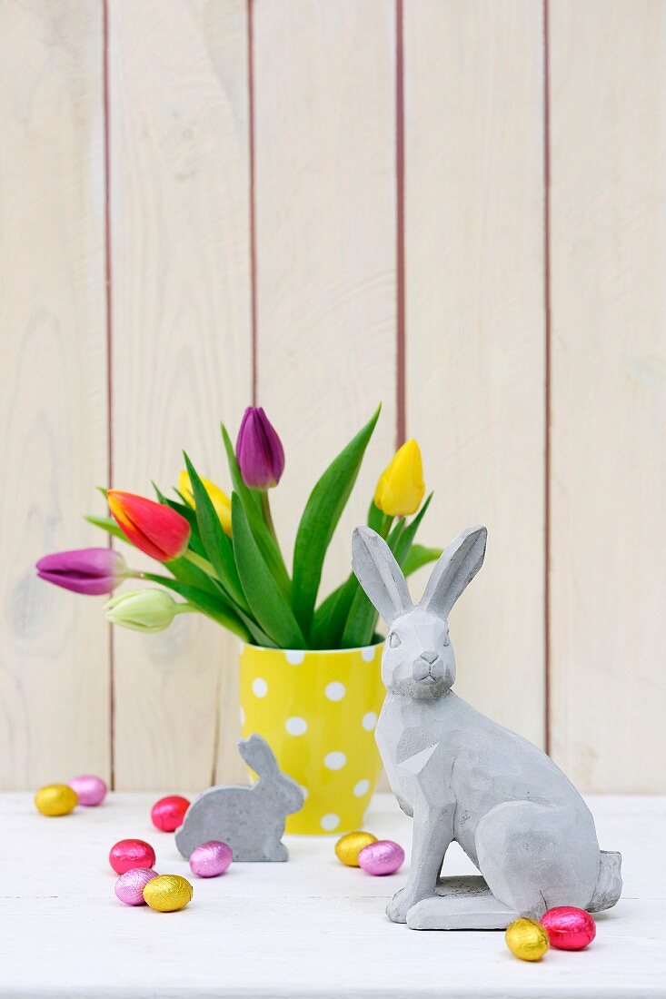 Easter arrangement of concrete rabbit ornament and vase of multicoloured tulips