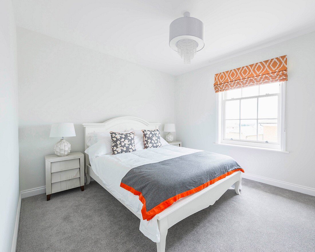 A white double bed with a headboard in front of lattice windows with retro orange blinds