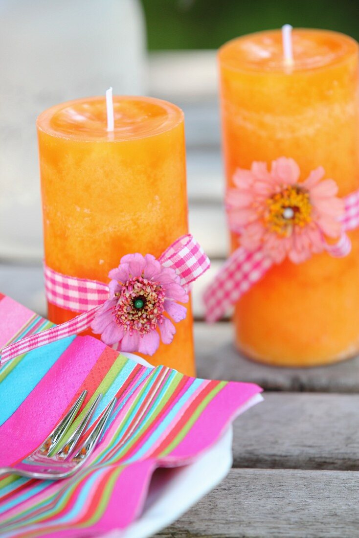 Pink striped napkins and two orange candles decorated with flowers nd ribbons