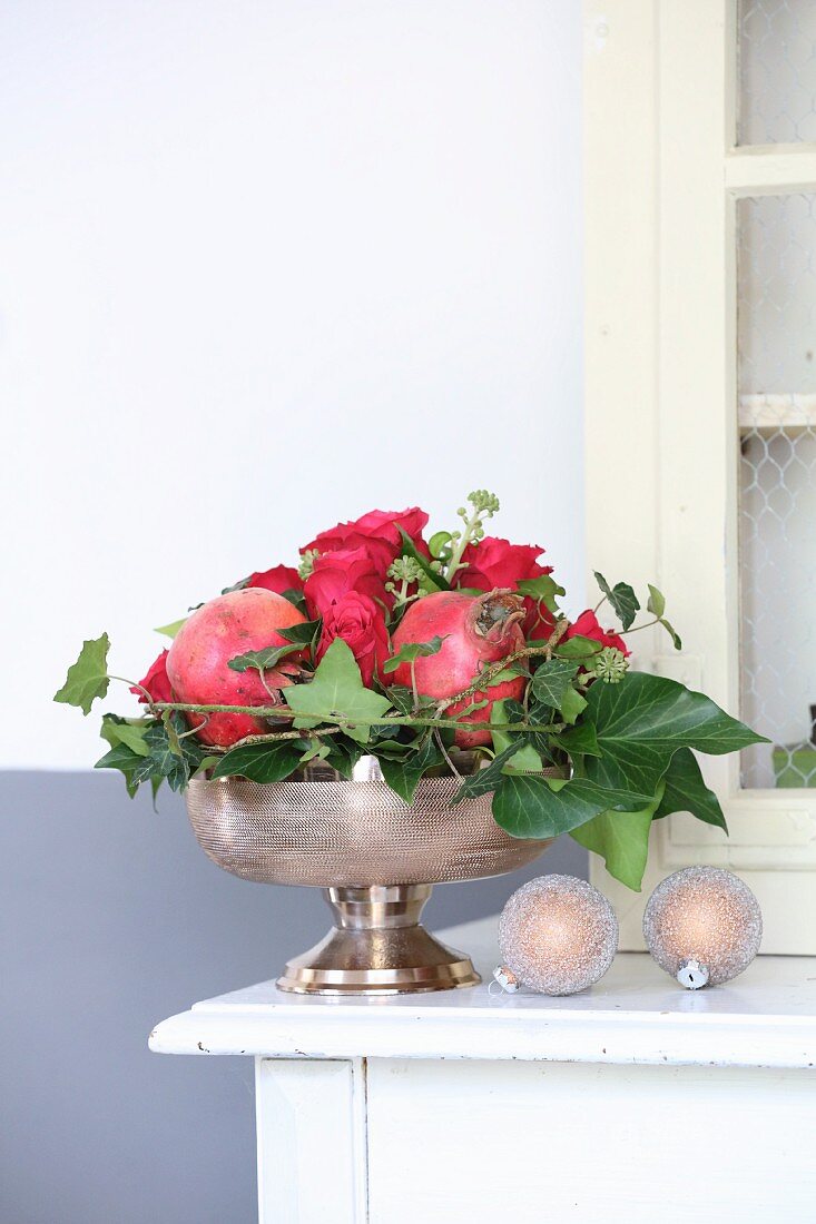 Festliches Weihnachtsgesteck mit Rosen, Granatäpfeln und Efeuranken in Silberschale