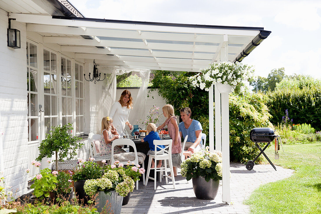 Familie am Tisch auf der überdachten Terrasse im sommerlichen Garten