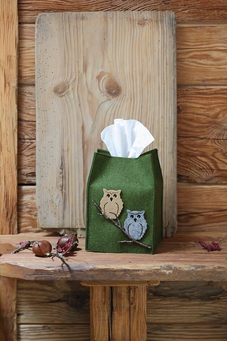 Dekorative, grüne Filzhülle mit Eulenmotiven für Kosmetiktücher auf rustikaler Holzbank