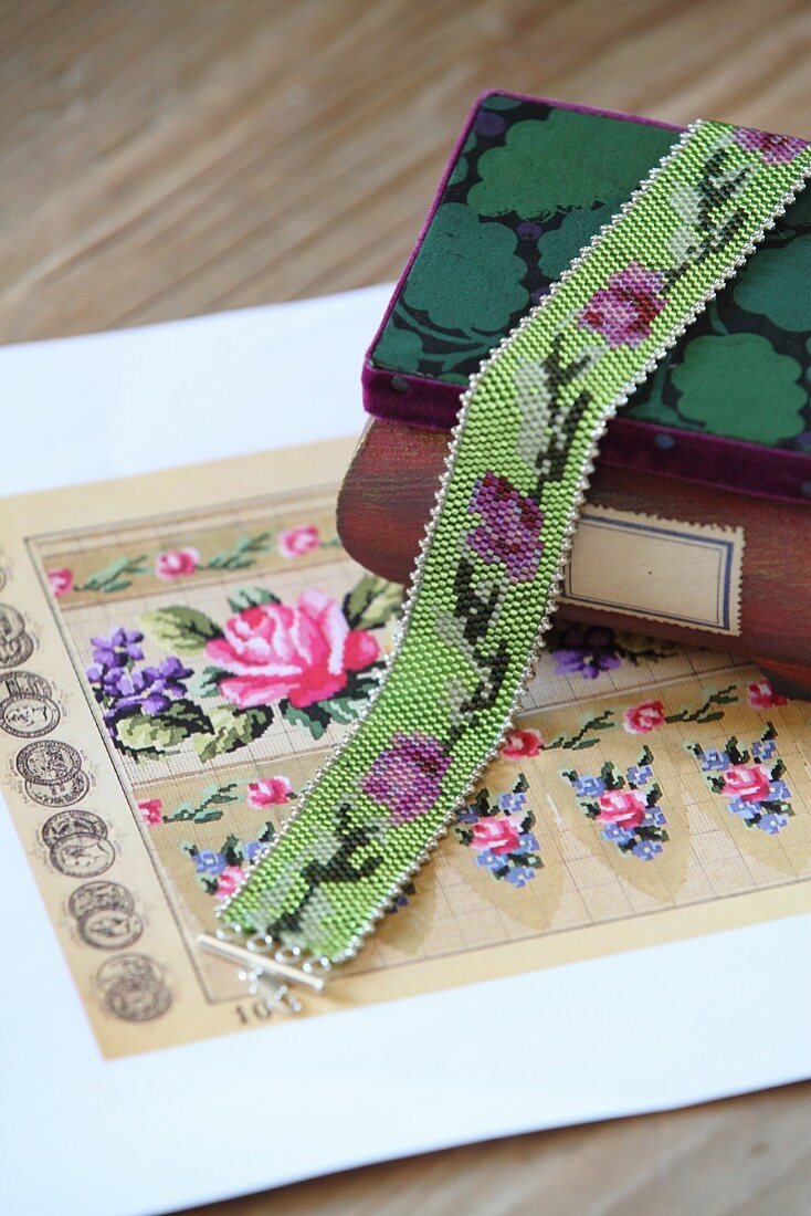 Glasperlen-Halsband über Holzschatulle und Fassvorlage mit Blumenmuster