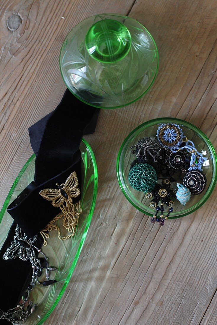 Glass-bead jewellery in green glass pot and decorated black ribbons in glass dish