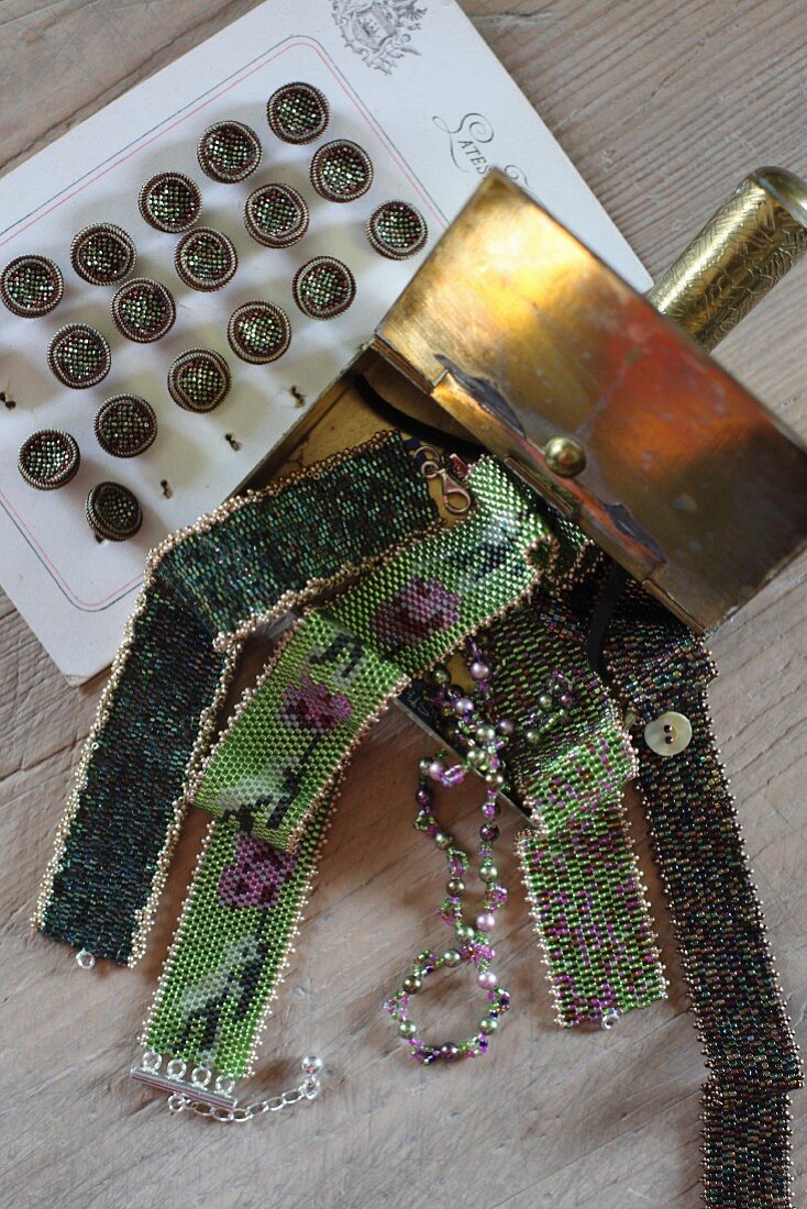 Verschiedene Glasperlen-Halsbänder in Metalldose neben Vintage Knöpfen
