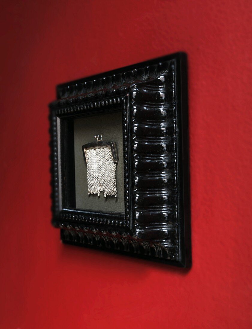 Elegante, silberfarbene Kettentasche in schwarzem Bidlerrahmen an roter Wand