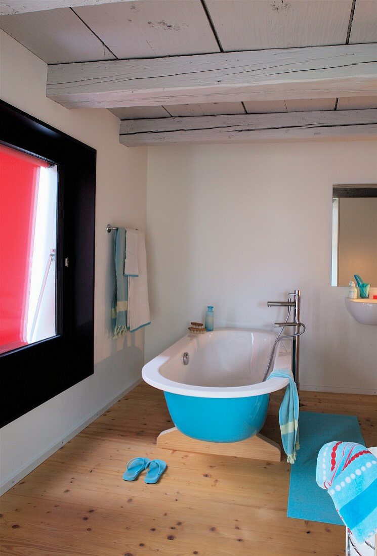 Blue free-standing bathtub in bathroom with wooden floor and wood-beamed ceiling