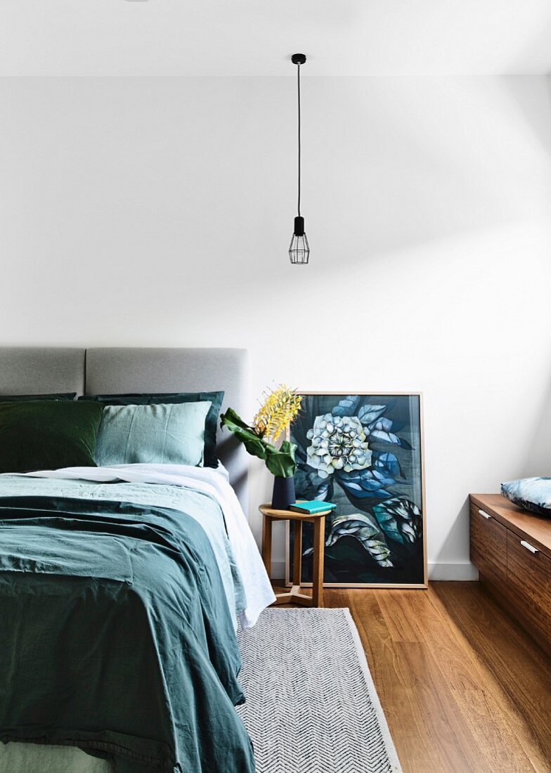Schlafzimmer mit Doppelbett, Pendelleuchte über Nachttisch und Bild mit Blumenmotiv