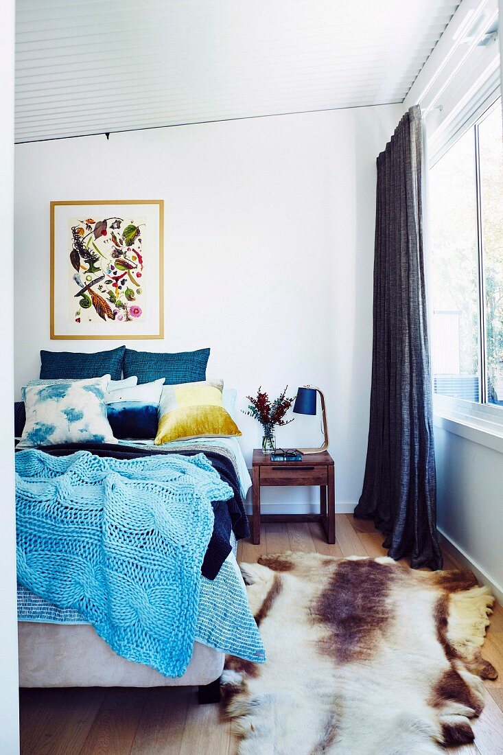 Blaue, gestrickte Tagesdecke auf Doppelbett und Tierfellvorleger im Schlafzimmer