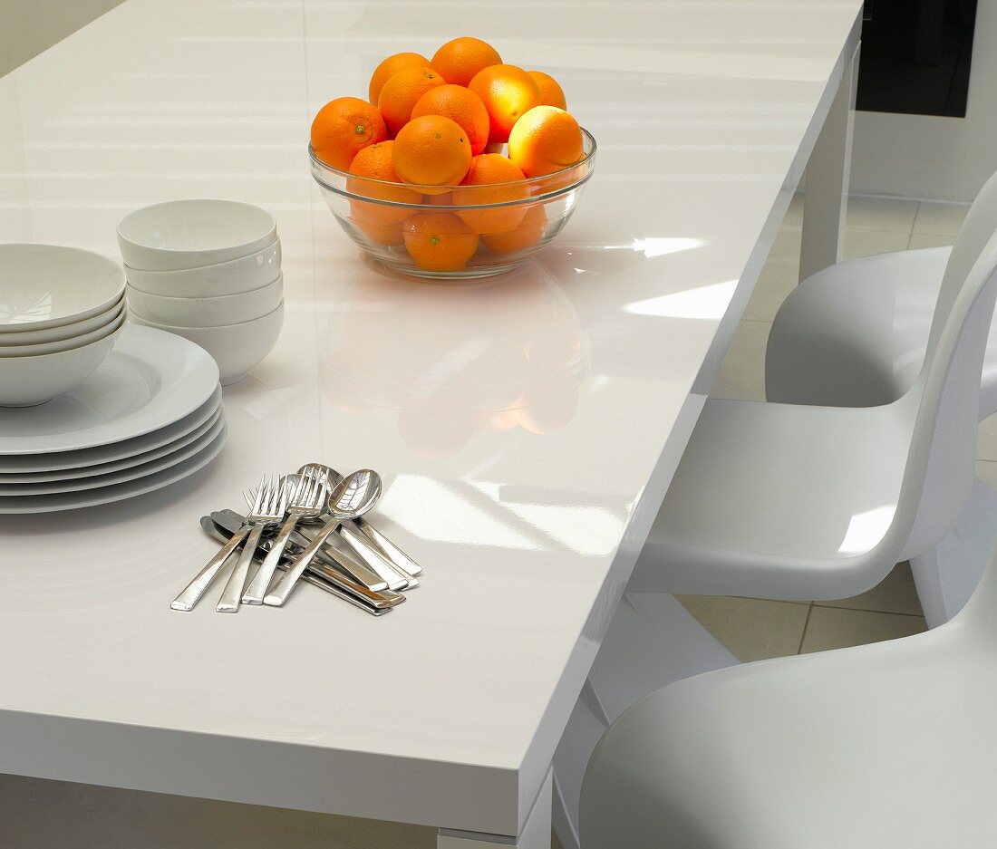 Glasschale mit Orangen, Geschirr und Besteck auf weißem Tisch