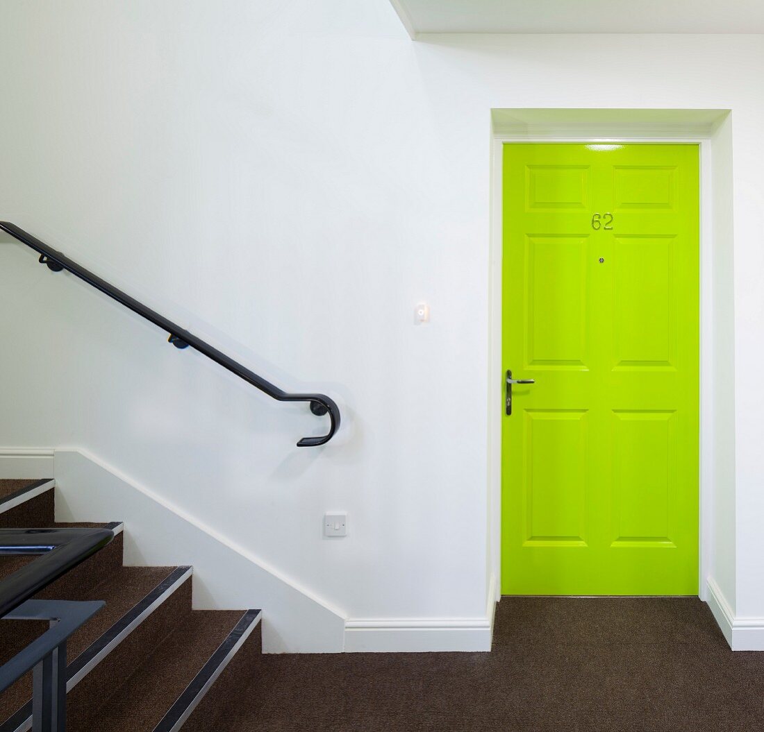 Neongrüne Kassettentür in weißem Treppenhaus mit braunem Teppichboden