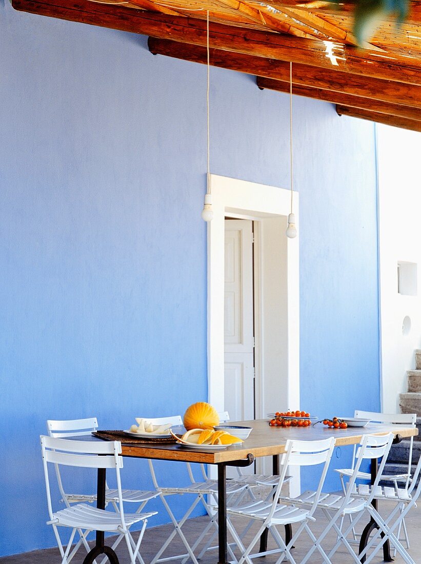Esstisch und weiße Stühle vor blauer Wand auf mediterraner Terrasse