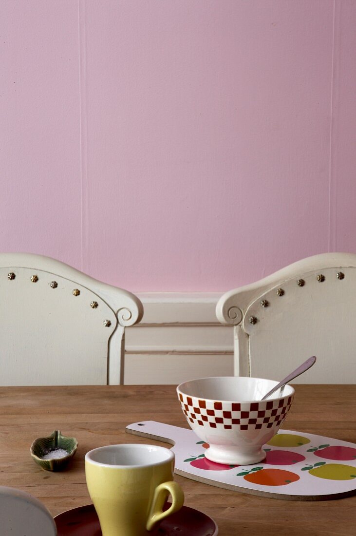 Schälchen und Schneidebrett auf Holztisch vor rosa Wand
