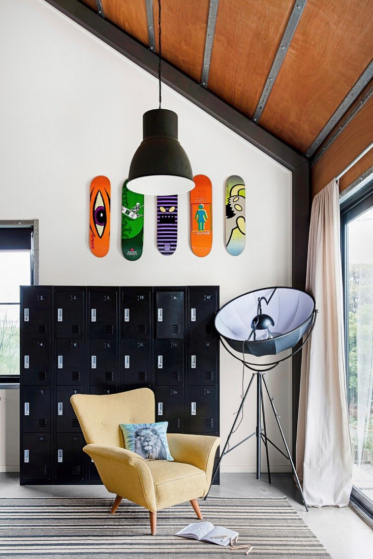 Black metal locker cabinet with colorful skateboards on the wall, yellow armchairs and photo lamp in front of the patio door