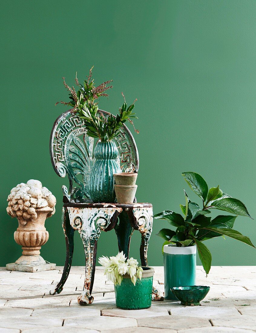Vintage Metallstuhl umgeben von Pflanzen und Skulptur vor grüner Wand