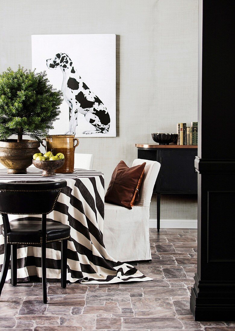 Conifers on table with black and white tablecloth, chairs, black sideboard and picture with Dalmatian motif on the wall