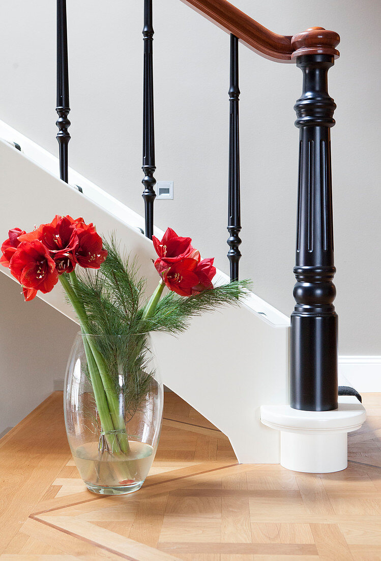 Bouquet of red amaryllis in glass vase next to staircase balustrade