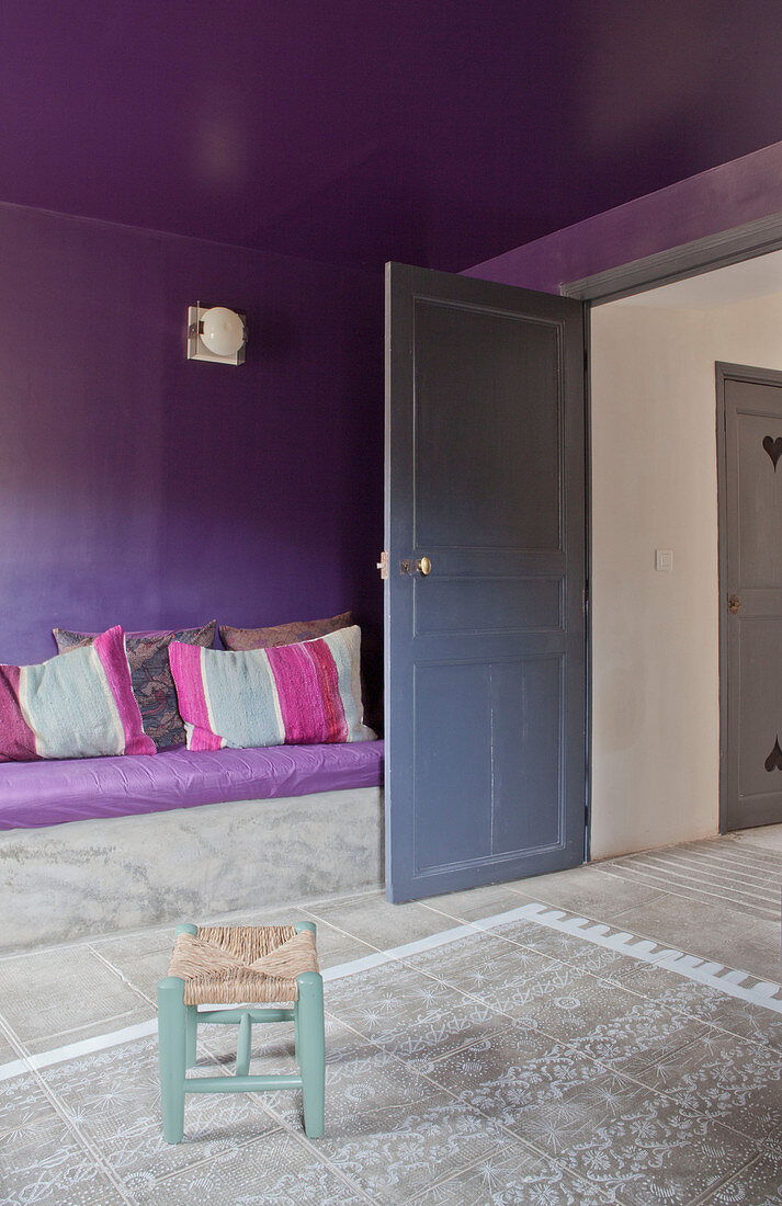Aufgemalter Teppich vor gemauertem Sofa an violetter Wand und Decke