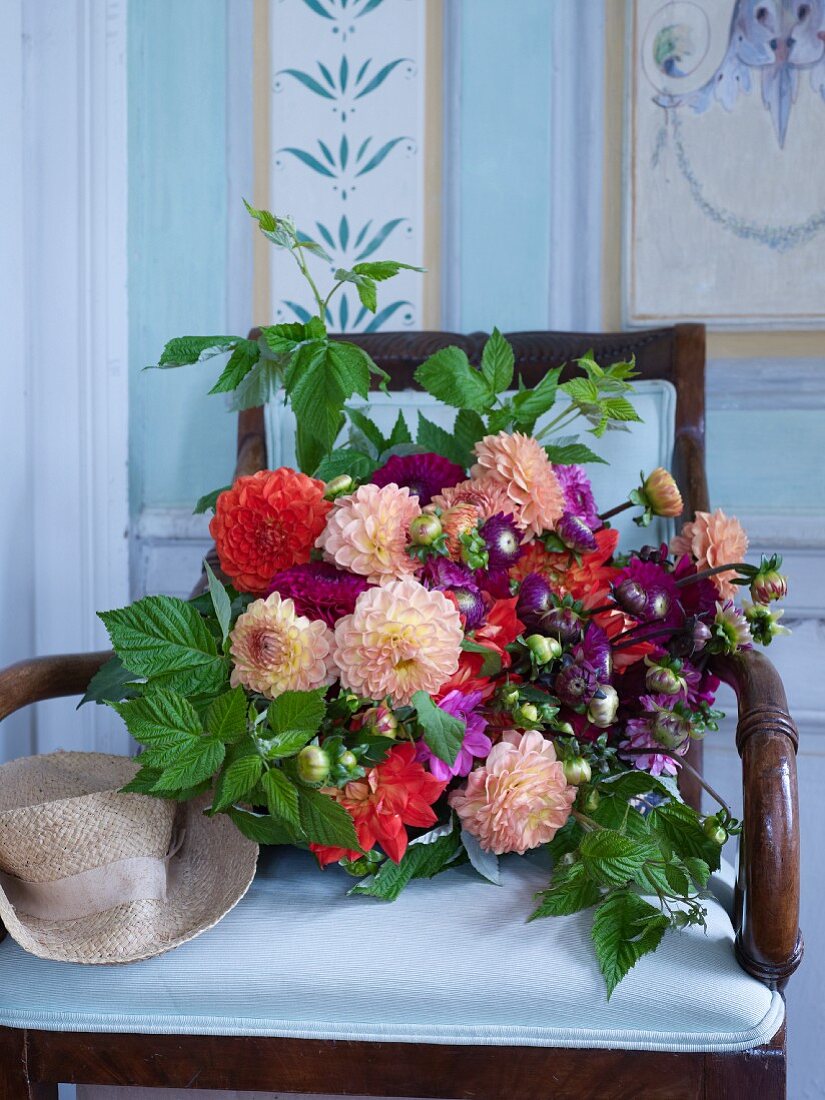 Üppiger Blumenstrauß mit Dahlien und Himbeerzweigen auf einem Stuhl