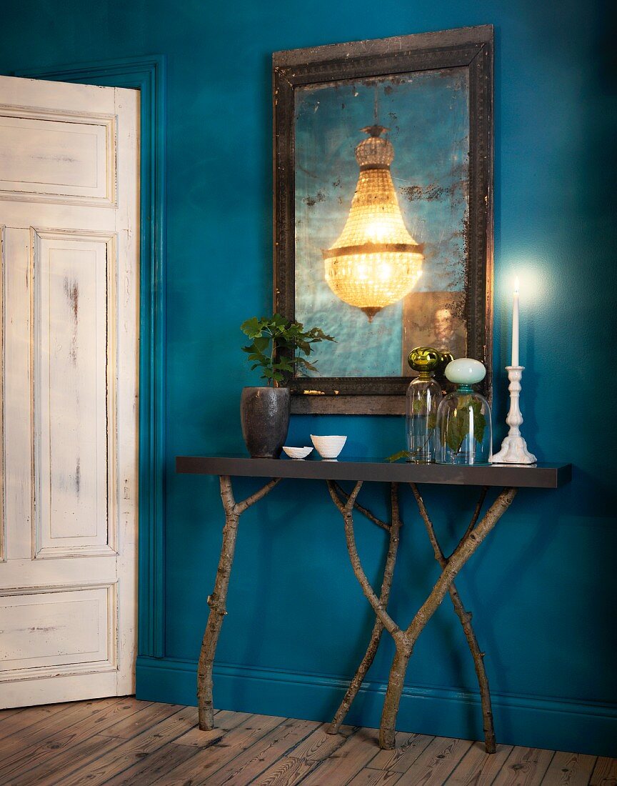Deep blue hallway with console table on branches as legs and chandelier reflected in mirror